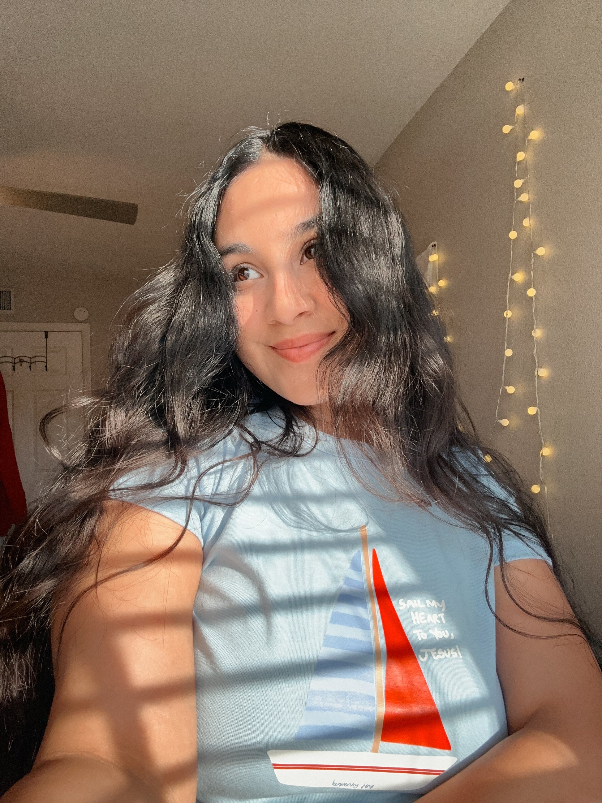 Person wearing a t-shirt with a sailboat design in a room with string lights.