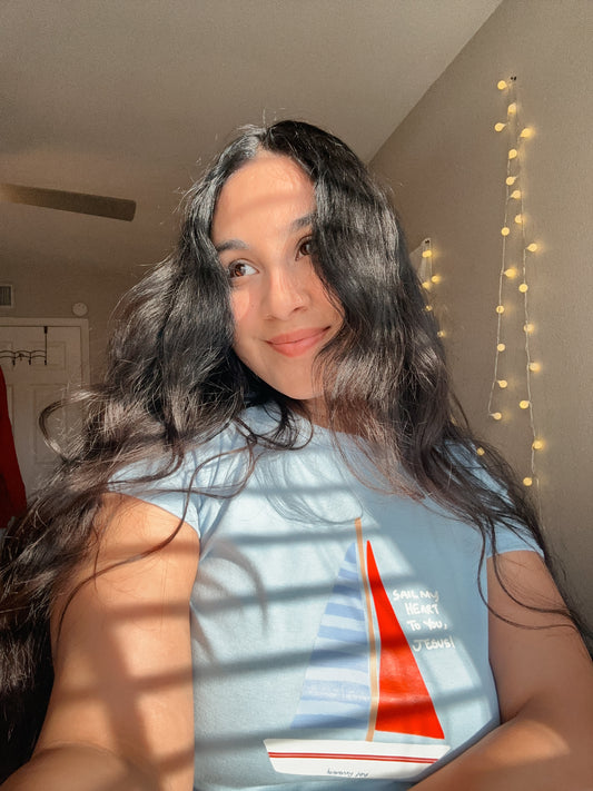 Person wearing a t-shirt with a sailboat design in a room with string lights.