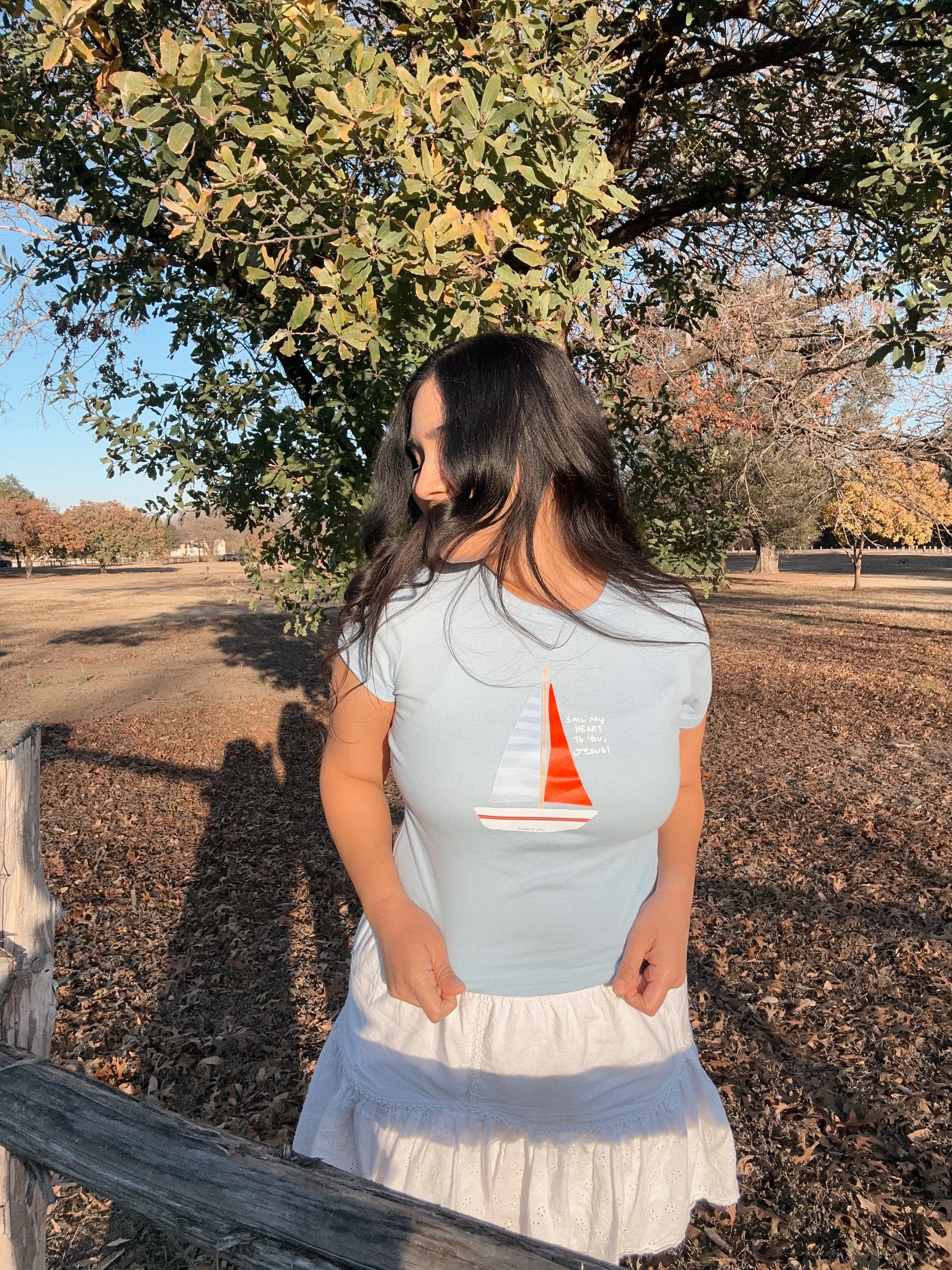 Woman wearing a light blue t-shirt with a sailboat design outdoors.